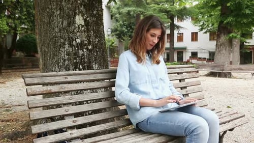 Young Woman Using Tablet on a Park Bench