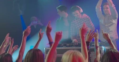 Energetic Crowd Dancing at Nightclub with DJs