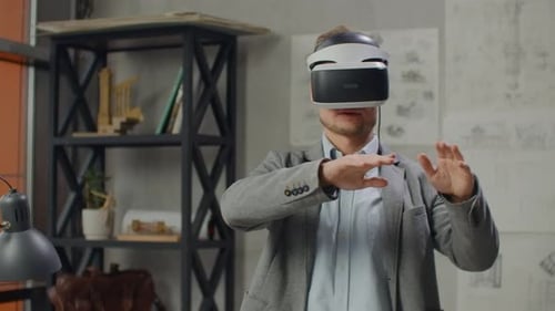 Young Man Designer in Office in Virtual Reality Helmet with Hands Makes Movements Imitating the Work