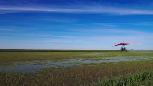 Powered Hang Glider Flies Over a Green Field