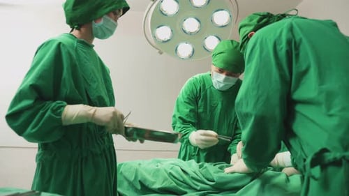 Asian professional medical team performing surgical operation in modern operating room in hospital.