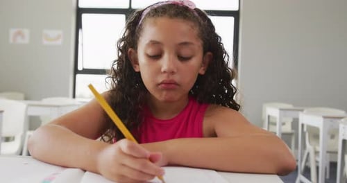 Video of happy biracial girl sitting at school desk and learning