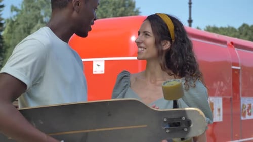 Young Couple with Skateboard Talking Near Food Truck