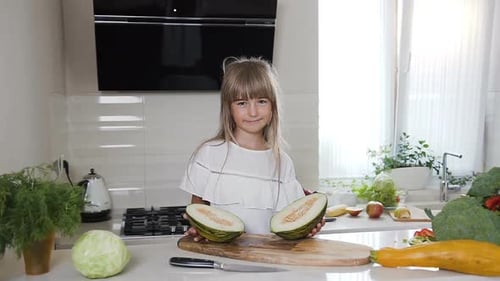 Jolie petite fille en robe blanche sur une planche de bois tient un melon vert coupé en deux