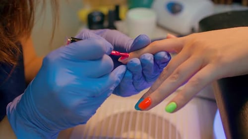 Unrecognizable Person in Gloves Paints Nails of Young Woman in Salon