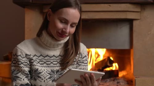 Woman Using a Digital Tablet Sits By the Fireplace