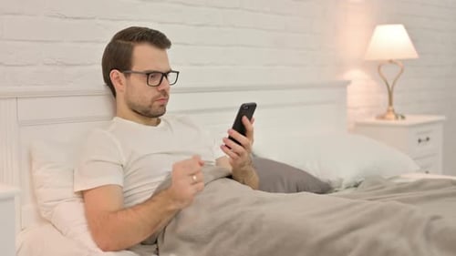 Man Lying in Bed Looking Shocked at Phone