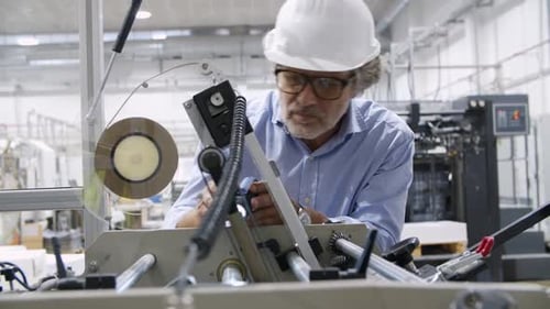 Focused Old Factory Engineer Inspecting Machine with Flashlight