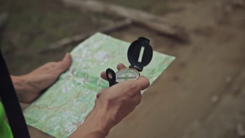 Slow Motion of a Young Tourist Man with a Road Card and a Compass in the Woods Searching for the