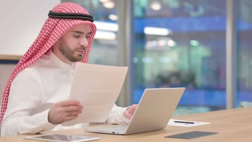 Serious Businessman Working on Laptop with Documents in Office