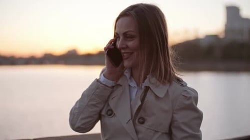 Woman Talking on Phone Near Water at Sunset