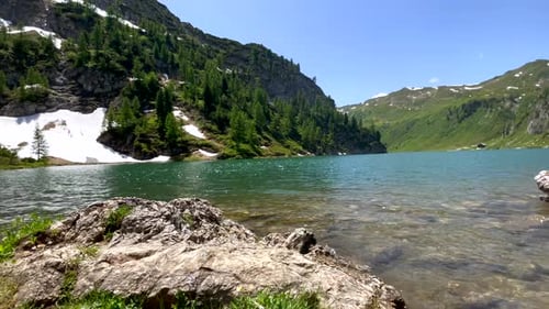 Panorama shot of idyllic mountain river surrounded by green mountains and snow on river shore - Clim