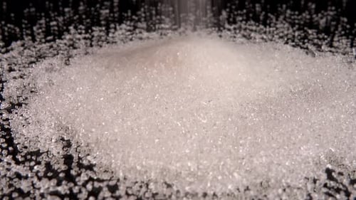 Falling grains of sugar on a black mirror background.