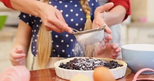 Child and Adult Adding Powder to Blueberry Pie