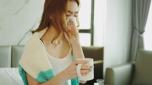 Woman Wipes Nose and Sips Drink in Bed