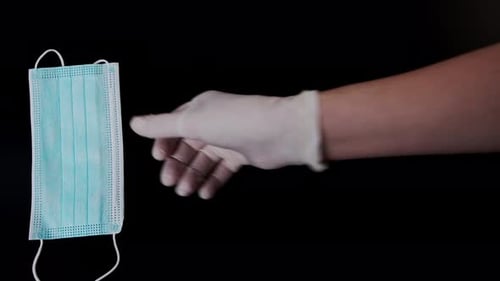 Gloved Hand Arranging Surgical Masks on Black Surface