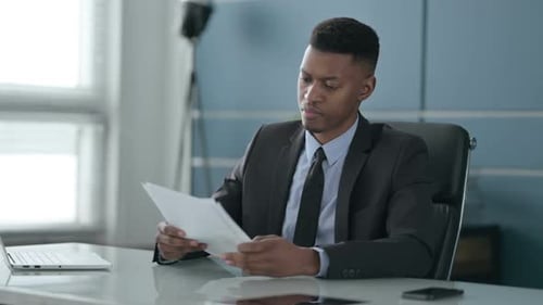 African Businessman Reading Reports while Sitting in Office