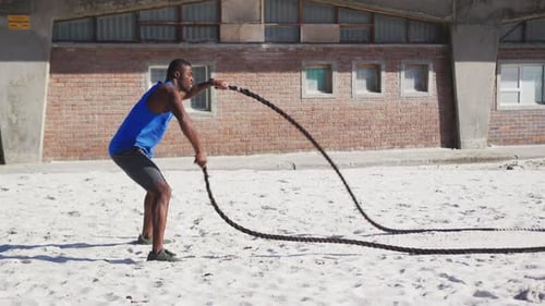 Fokussierter Afroamerikaner trainiert mit Kampfseilen im Freien am Strand