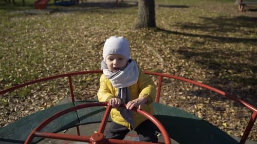 Adorable infant son playing at merry-go-round in public playground, Zagreb.