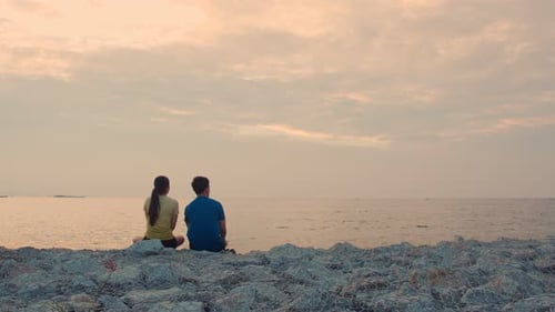 Couple Watching Sunset on Rocky Ocean Shore