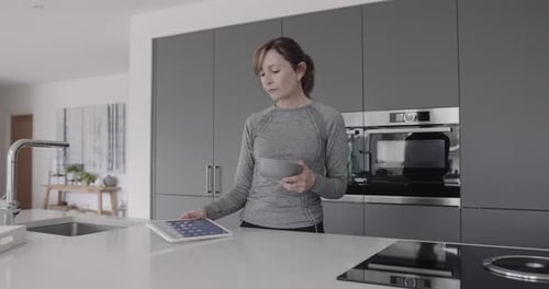 Woman with Tablet Eating Food in Modern Kitchen