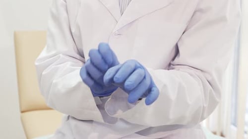 Doctor Puts On Blue Medical Gloves in Clinic