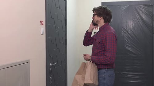 Un repartidor de pie en la puerta del apartamento de un cliente con paquetes de comida.