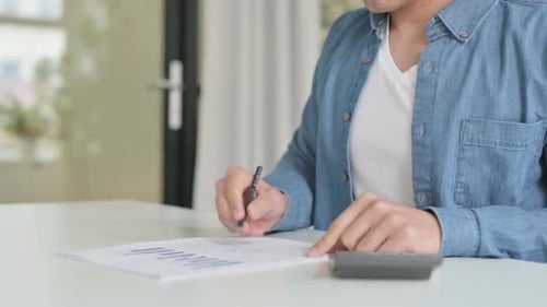 Nahaufnahme eines Mannes, der Berechnungen macht und auf Papier schreibt
