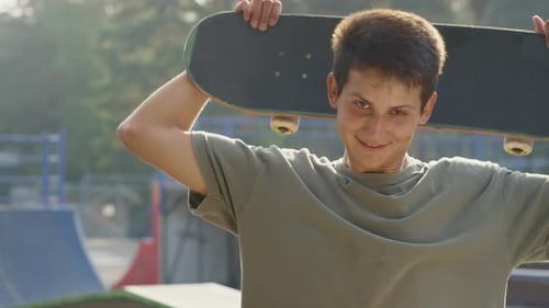 Teenager Holds Skateboard on Shoulders at Skate Park