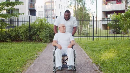 Caregiver Pushing Senior in Wheelchair Through Park