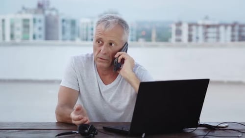 Man Talking on Phone While Working on Laptop
