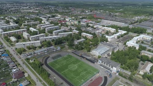Aerial view of stadium in city with low houses and factory at background