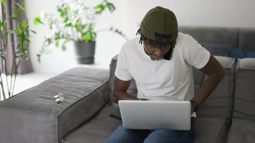 Young Man Works on Laptop and Talks on Phone