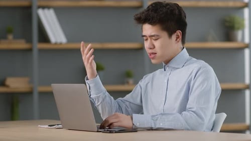 Junge asiatische Büroangestellte, die per Laptop-Chat Videokonferenzen mit ausländischen Partnern unterhält, sitzt gemütlich
