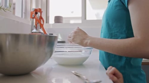 Woman Cracking Egg into Bowl of Milk in Kitchen