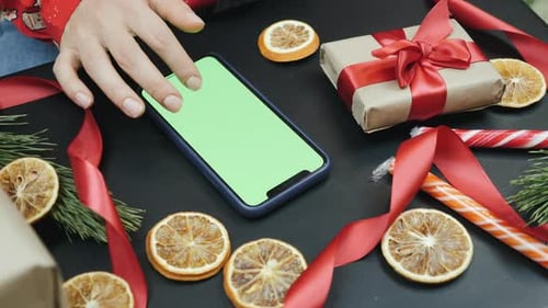 Woman is searching xmas gifts online on smartphone with green screen. Christmas concept