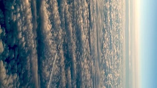 Flying airplane above clouds leaving condensation vapor air trail in blue sky. VERTICAL format zoom