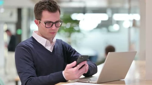 Young Adult Using Phone and Laptop at Workplace