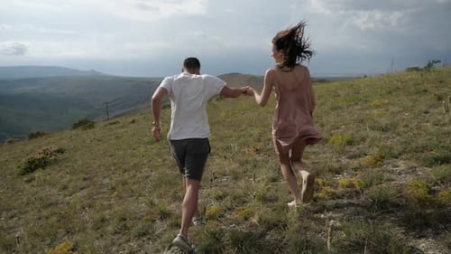 Happy Couple Running Hand-in-Hand Up Grassy Hill