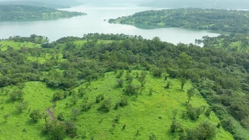 Approaching a huge water reservoir flying over a lush green jungle during a monsoon afternoon