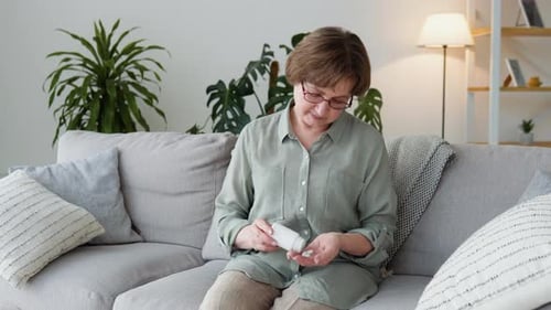 Senior Woman Taking Pills on Couch at Home