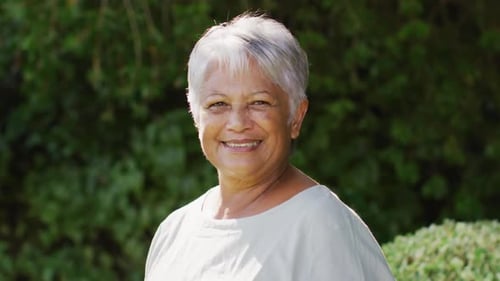 Video of happy biracial senior woman looking at camera in garden