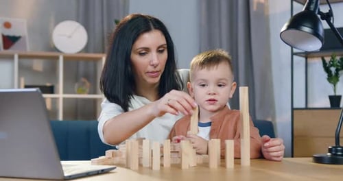 Mujer que ayuda a construir una torre de madera con bloques junto con su pequeño y lindo hijo