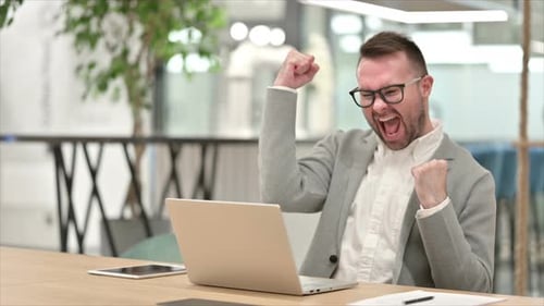 Man Celebrating Success at Office Workplace Using Laptop