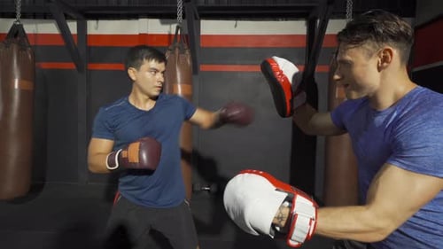 Caucasian man doing boxing training with trainer or coach, combat punches in boxing sport club
