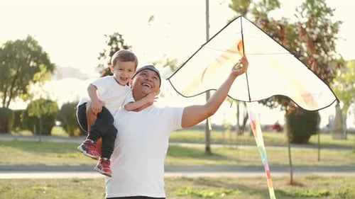 Father and Son Flying a Kite in City Park on Sunset