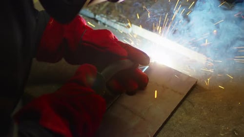 Trabajador industrial en máscara protectora usando una moderna máquina de soldadura para soldar construcciones metálicas en