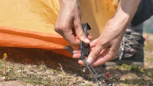 Une personne attache une tente jaune à la main avec une boucle et s'en va