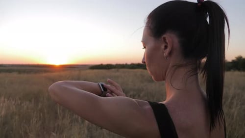 Woman Checking Smartwatch in Field at Sunrise