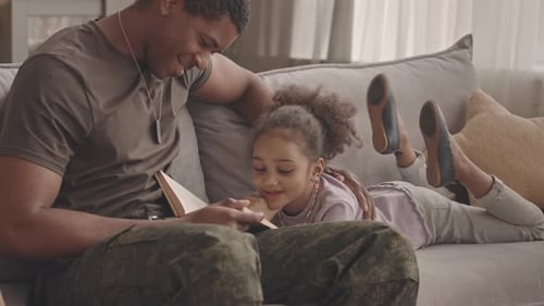 Military Father and Daughter Reading Book on Sofa
